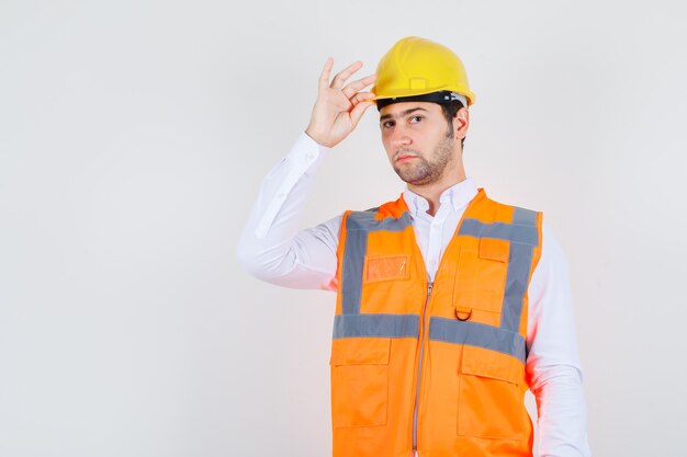 Homem Construtor segurando seu capacete na camisa, jaqueta e olhando sério, vista frontal.