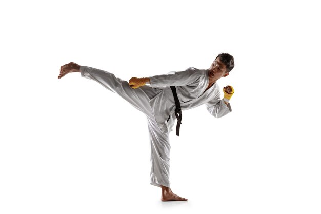 Homem coreano confiante no quimono, praticando combate corpo a corpo, artes marciais. Jovem lutador masculino com treinamento de faixa-preta isolado na parede branca. Conceito de estilo de vida saudável, esporte.