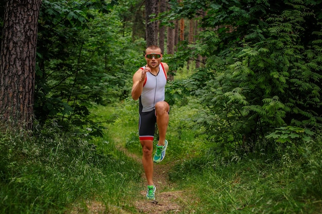 Homem correndo em roupas esportivas na floresta verde de verão.