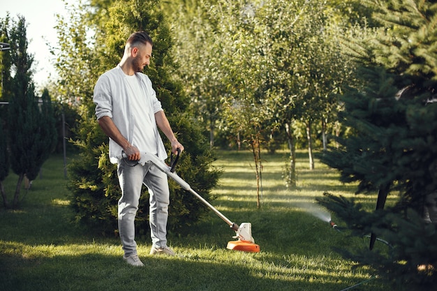 Homem cortando grama com o movedor de gramado no quintal. Homem com uma camisa.