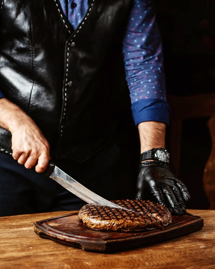Foto grátis homem cortar bife em forma redonda, usando luvas pretas