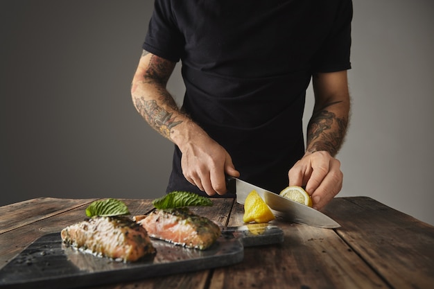 Homem cozinha refeição saudável, corte limon atrás decorado com folha de hortelã dois pedaços crus de salmão em molho de vinho branco com especiarias e ervas apresentados no deck de mármore preparado para grelhar