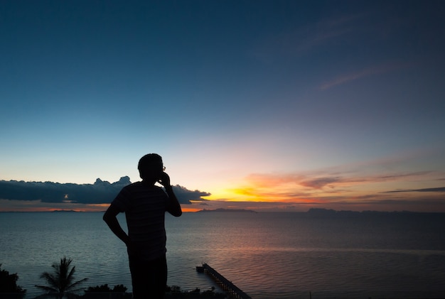 Homem da silhueta que fala no telefone com opinião do por do sol.