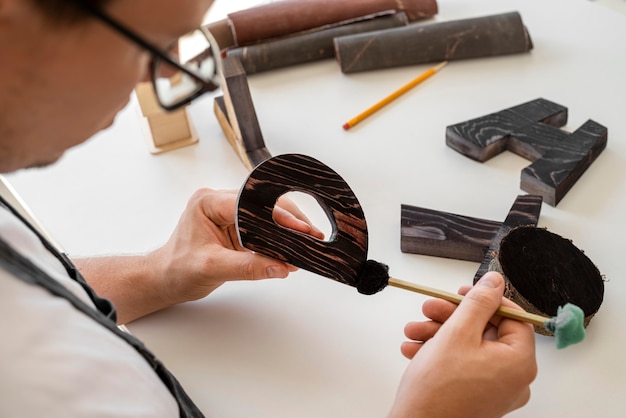 Homem de alto ângulo pintando letras de madeira