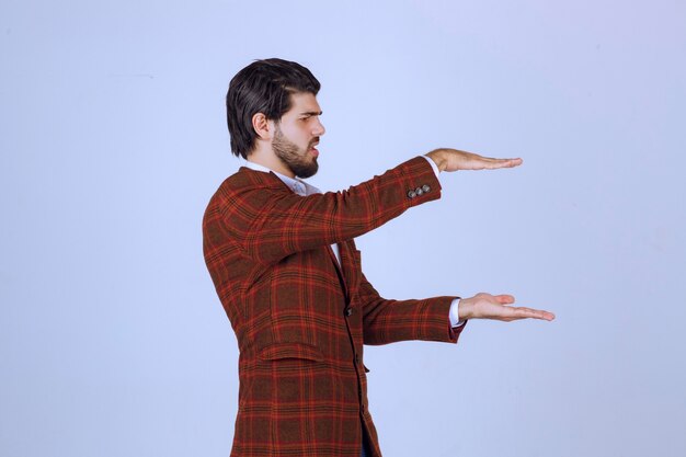 Foto grátis homem de blazer marrom, mostrando a altura de um objeto estimado.