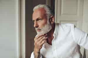 Foto grátis homem de cabelo branco e camisa posando pensativamente em apartamento claro