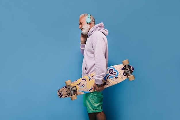 Foto grátis homem de cabelo branco em uma roupa de estilo de rua ouvindo música e segurando uma prancha de skate