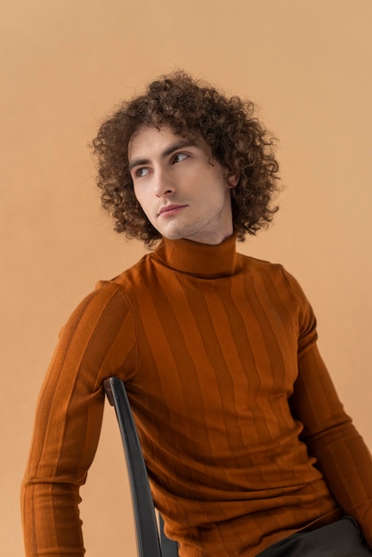 Homem de cabelos cacheados com blusa marrom posando