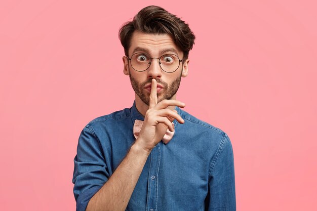 Homem de cabelos escuros vestindo gravata borboleta rosa e camisa jeans