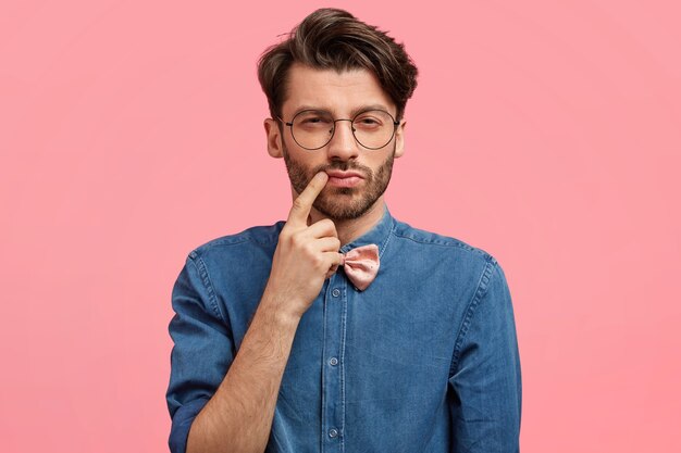 Homem de cabelos escuros vestindo gravata borboleta rosa e camisa jeans