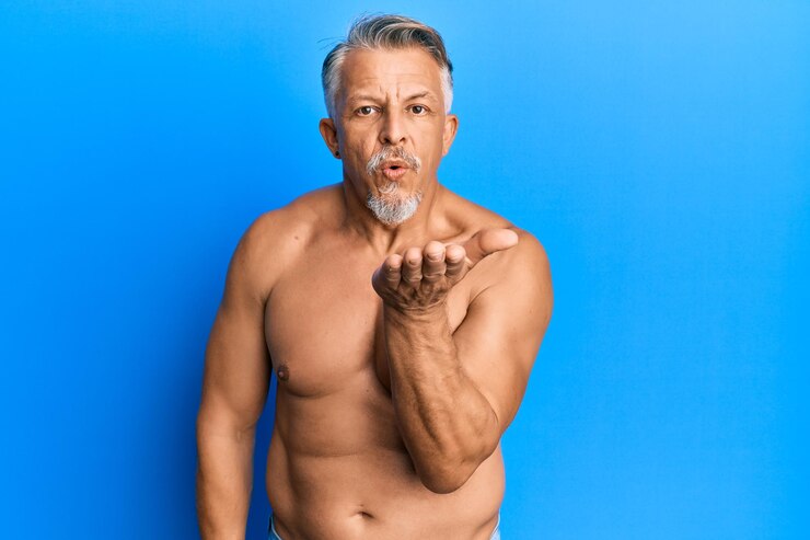 Foto grátis homem de cabelos grisalhos de meia-idade sem camisa olhando para a câmera mandando um beijo com a mão no ar sendo adorável e sexy. expressão de amor.