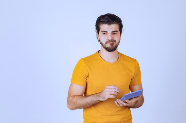 Homem de camisa amarela, calculando algo na calculadora.