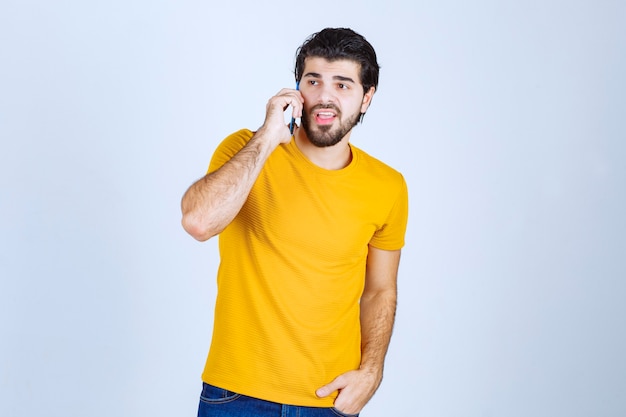 Homem de camisa amarela, falando ao telefone.