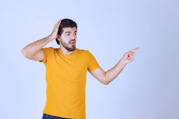 Homem de camisa amarela, mostrando algo à direita.