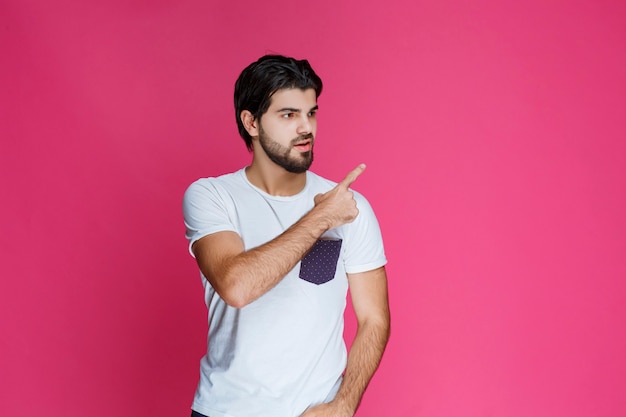 Foto grátis homem de camisa branca, apontando e apresentando algo no lado direito.