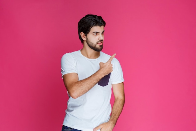 Foto grátis homem de camisa branca, apontando e apresentando algo no lado direito.