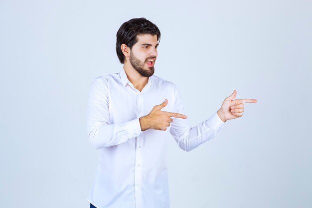 Homem de camisa branca, apontando para algo à direita.