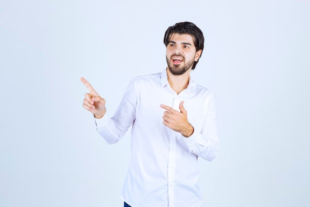 Homem de camisa branca apontando para algum lugar à esquerda com emoções de rosto.