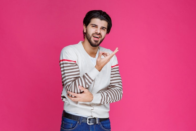 Homem de camisa branca apontando para algum lugar e apresentando alguém ou apenas mostrando a direção.