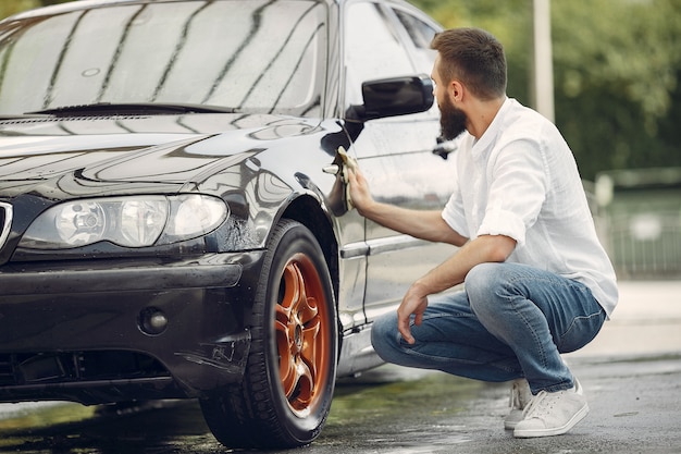 Homem de camisa branca limpa um carro em uma lavagem de carro