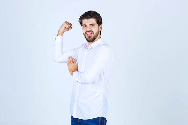 Homem de camisa branca, mostrando os músculos do braço e o punho.