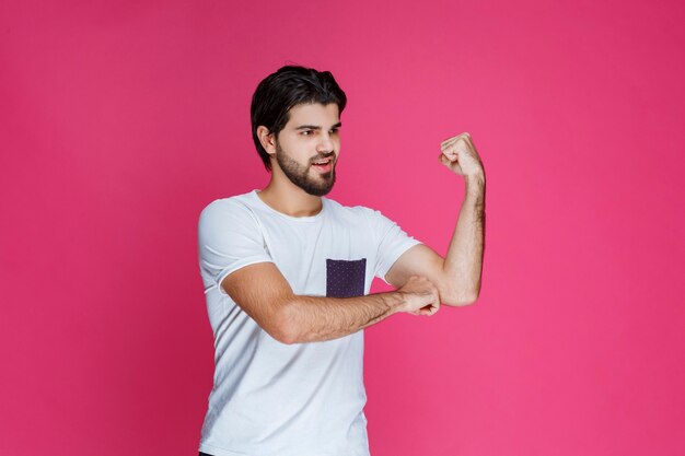 Homem de camisa branca, mostrando os músculos do punho e bíceps.