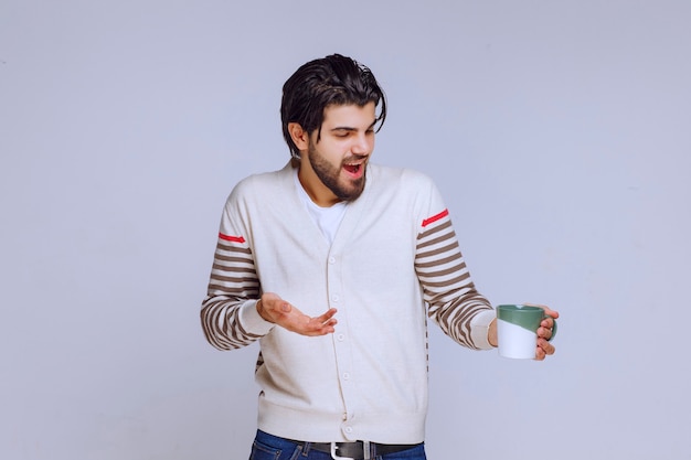 Homem de camisa branca segurando e posando com uma caneca de café.