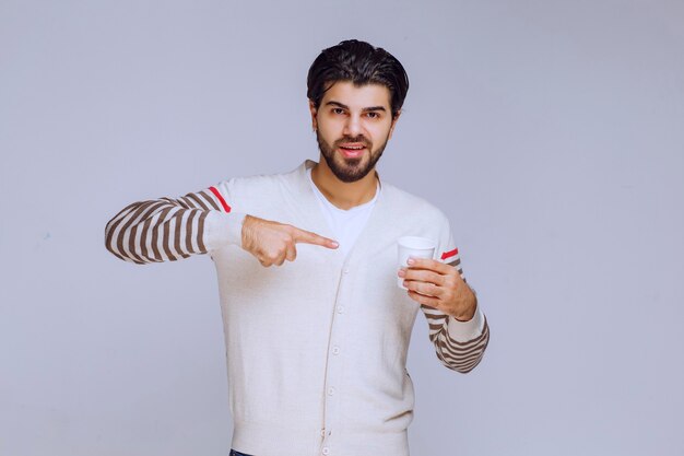 Homem de camisa branca segurando uma xícara de café e apontando para ela.