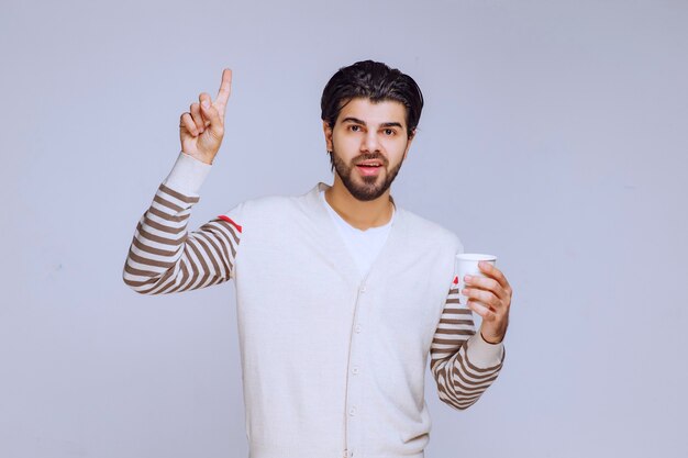 Homem de camisa branca segurando uma xícara de café e gostando.