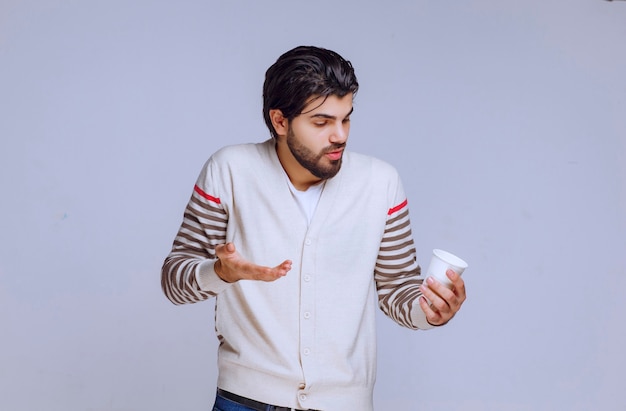 Homem de camisa branca segurando uma xícara de café e parece pensativo.