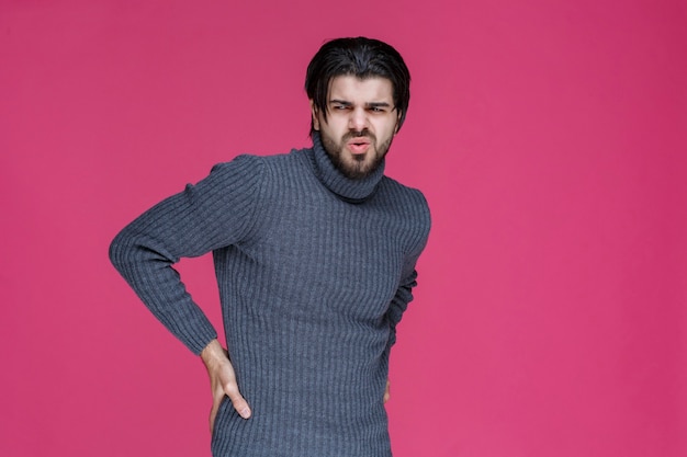 Homem de camisa cinza de mãos dadas na cintura como se estivesse com dor nas costas.