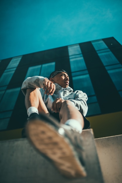 Homem de camisa listrada branca e preta e jeans azul sentado em um banco de concreto marrom