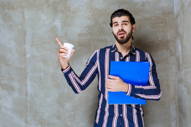 Homem de camisa listrada segurando uma pasta azul e um copo descartável branco