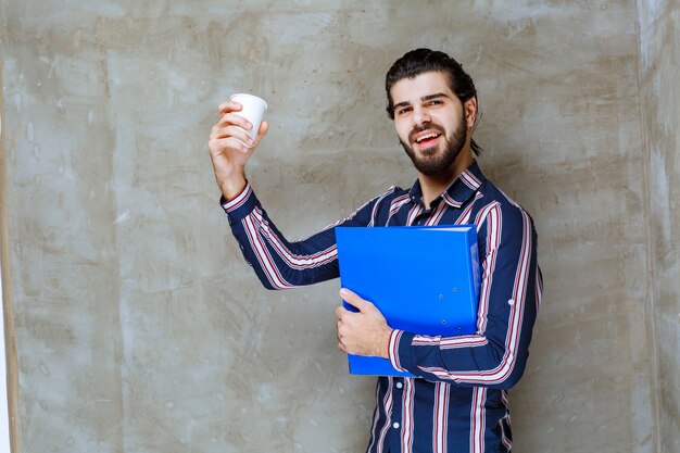 Homem de camisa listrada segurando uma pasta azul e um copo descartável branco