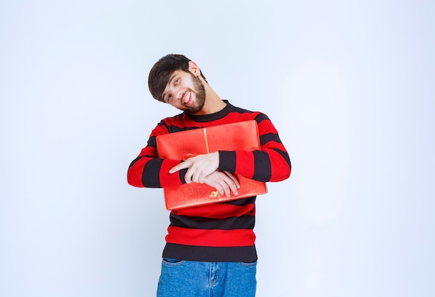 Foto grátis homem de camisa listrada vermelha segurando uma caixa de presente vermelha e abraçando-a com força e não quer compartilhar com ninguém.