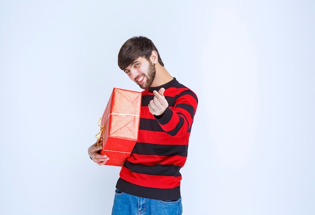 Foto grátis homem de camisa listrada vermelha, segurando uma caixa de presente vermelha e pedindo pagamento.