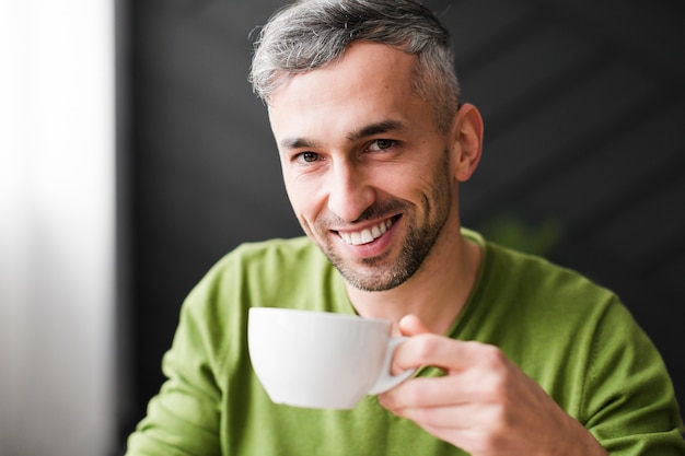 Homem de camisa verde sorri e segure a xícara de café