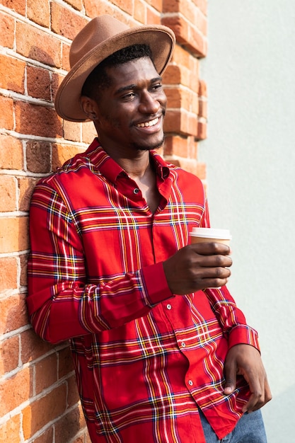 Homem de camisa vermelha encostado na parede e segurando um café