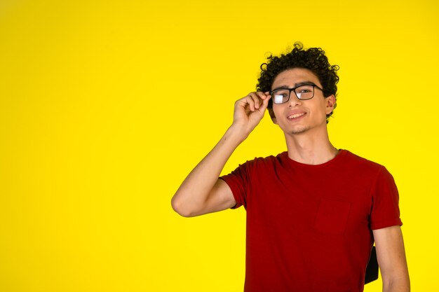 Homem de camisa vermelha, segurando os óculos e sorrindo.