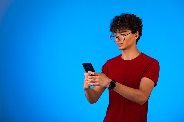 Homem de camisa vermelha tirando selfie em um smartphone em azul