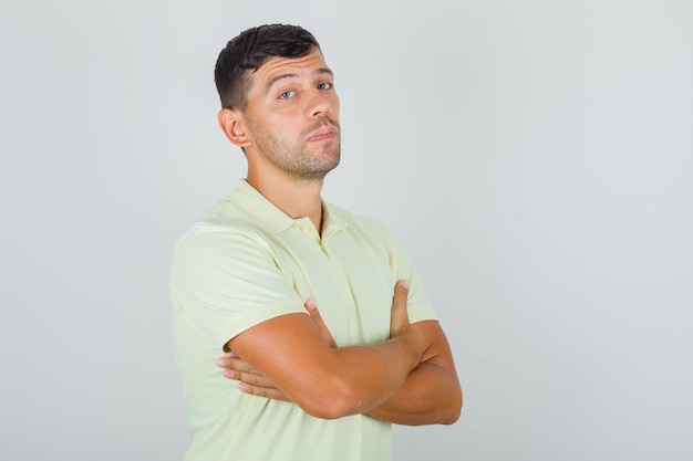 Foto grátis homem de camiseta amarela em pé com os braços cruzados e parecendo decidido