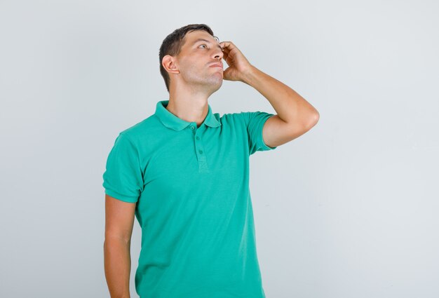 Homem de camiseta olhando para cima segurando a mão no rosto e olhando pensativo, vista frontal.