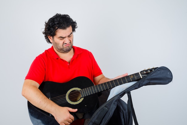 homem de camiseta vermelha tirando o violão do estojo e parecendo pensativo