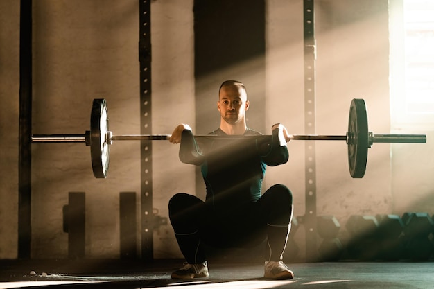 Homem de construção muscular se exercitando com barra no treinamento cruzado em uma academia