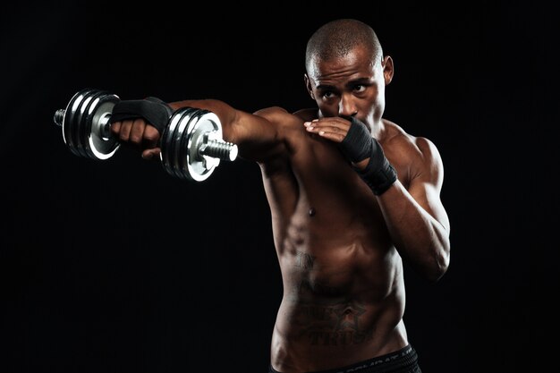Homem de esportes afro-americanos posando como uma luta com halteres