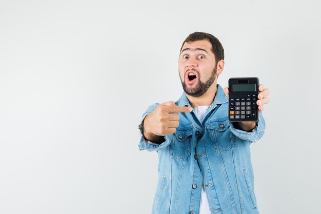 Homem de estilo retro apontando para calculadora em jaqueta, camiseta e parecendo perplexo. vista frontal. espaço para texto