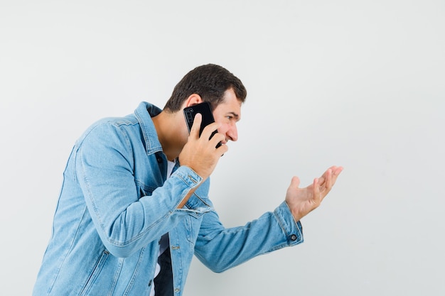 Homem de estilo retro com jaqueta, camiseta explicando algo no telefone e parecendo focado.