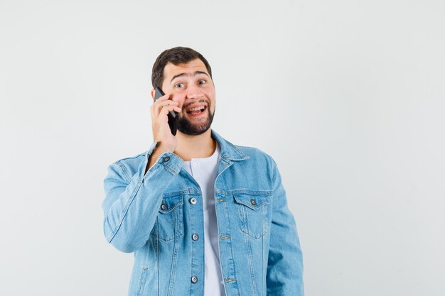 Homem de estilo retro com jaqueta, camiseta, falando no telefone e parecendo feliz, vista frontal.