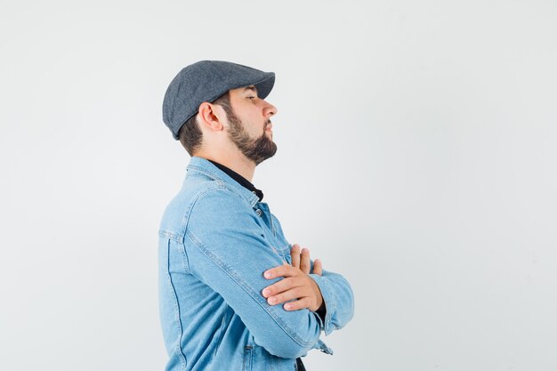 Homem de estilo retro em pé com os braços cruzados na jaqueta, boné.