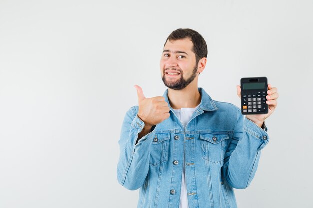 Homem de estilo retro mostrando a calculadora enquanto aparecia o polegar na jaqueta, camiseta e olhando otimista, vista frontal. espaço para texto